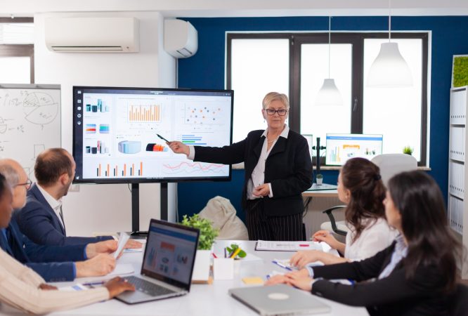 Senior woman company leader brainstorming in conference room Corporate staff discussing new business application with colleagues looking at screen